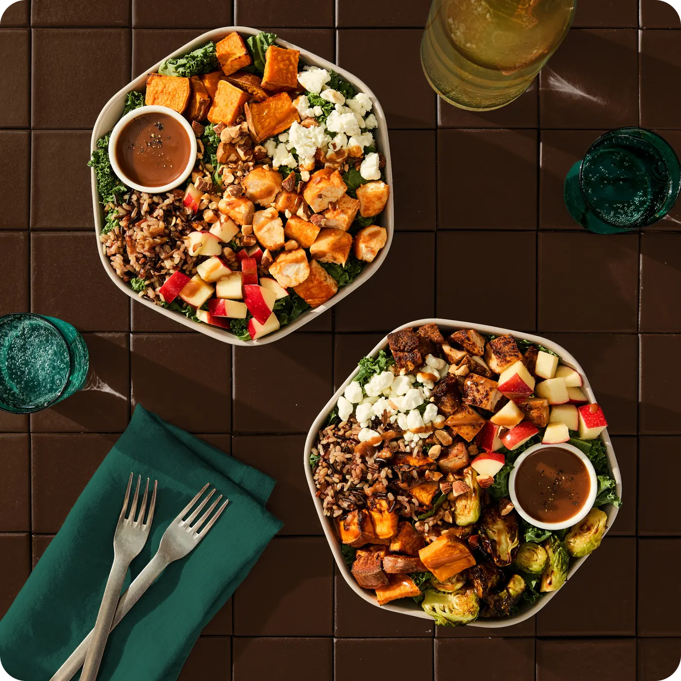 Two Sweetgreen fall bowls set for dinner with sweet potatoes, brussels sprouts, apples, and goat cheese