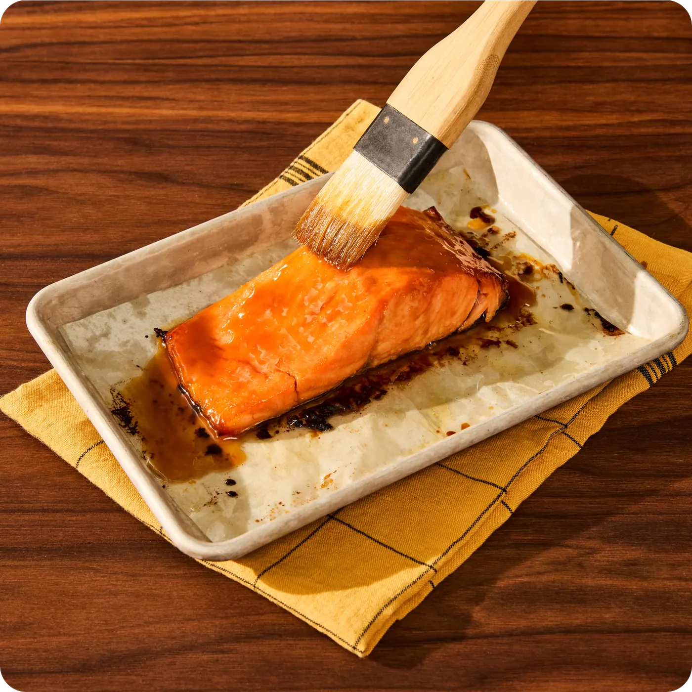 A fillet of Sweetgreen miso glazed salmon being brushed with maple glaze on a roasting tray