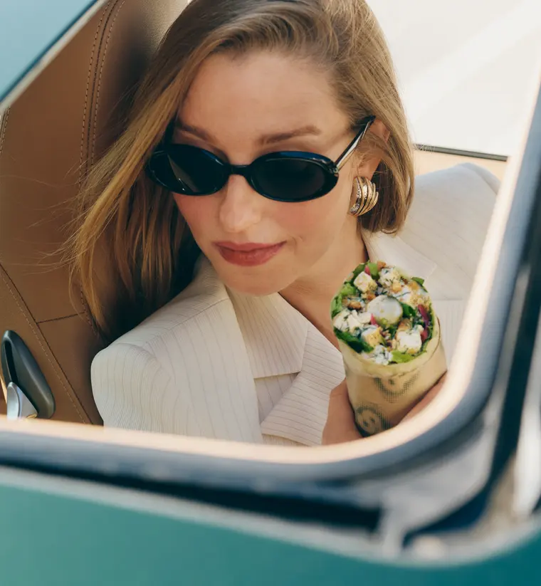 Molly Baz in sunglasses leaning out of a car window holding one of her wraps